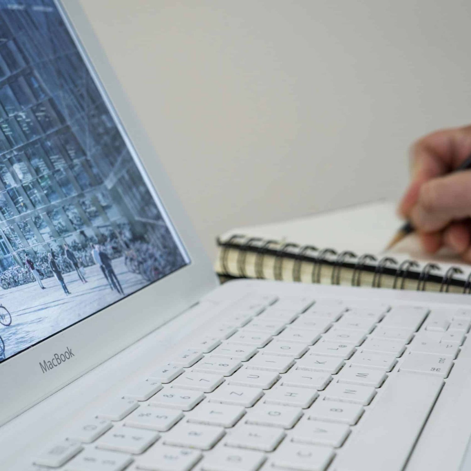 An open laptop and a writing pad with someone taking notes